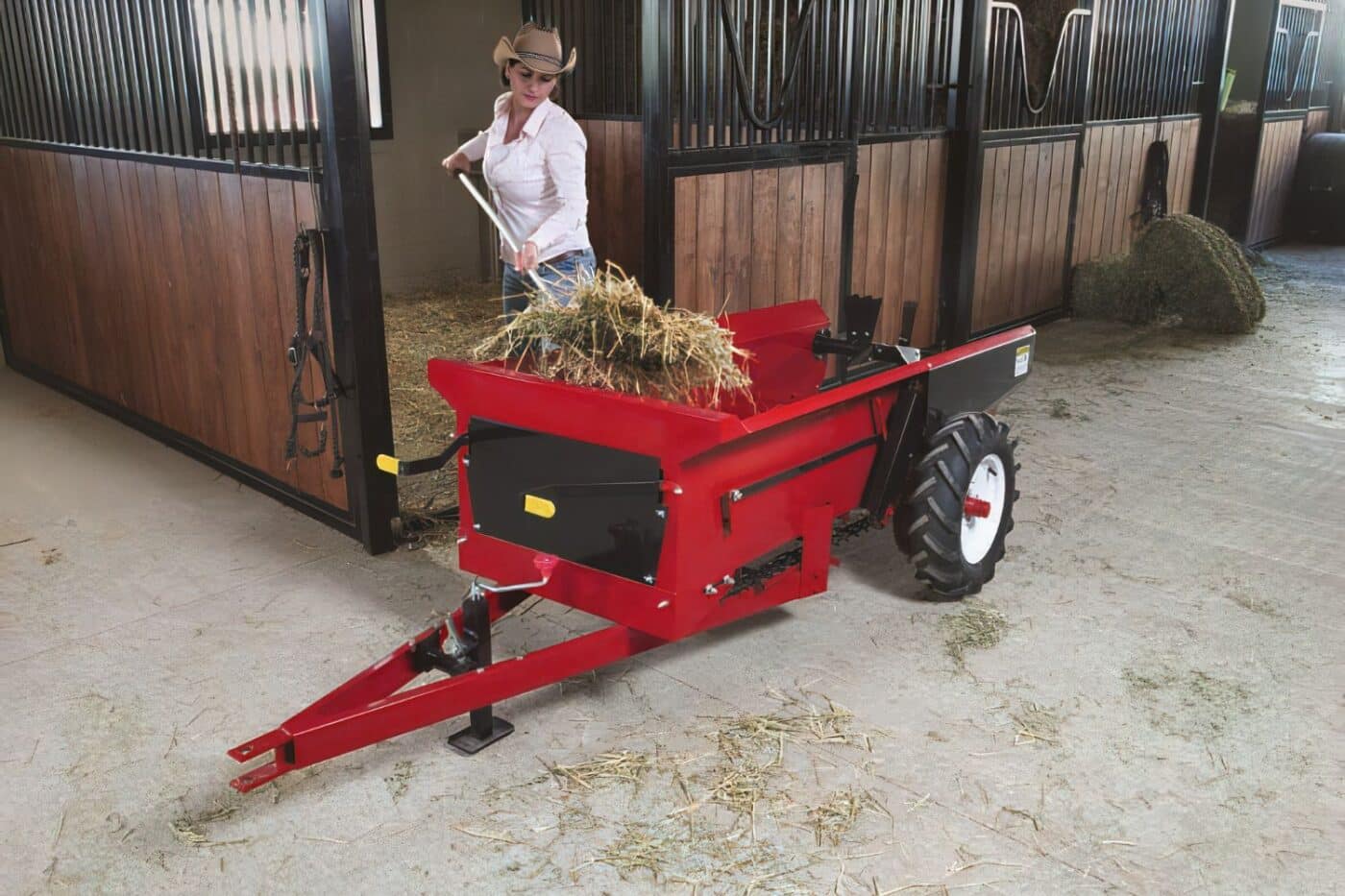 25 G Farmco Compact Manure Spreader being loaded by a woman standing in the doorway of a horse stall