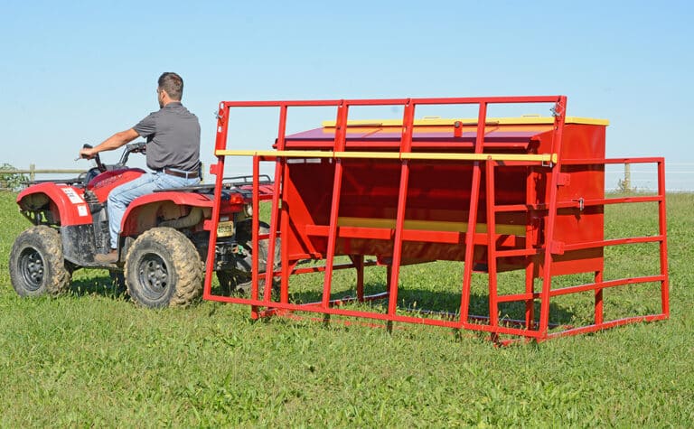 Man driving ATV pulling red creep feeder for calves